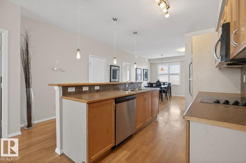 Open-concept kitchen featuring wood-finish flooring, light wood cabinetry, a stainless steel dishwasher, and a breakfast bar with pendant lighting - 614 10503 98 Avenue, Edmonton, AB - Indoor Photo Showing Kitchen With Double Sink