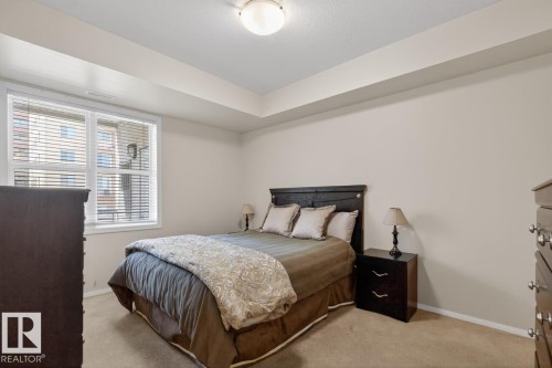Carpeted bedroom featuring a large window with horizontal blinds, neutral wall paint, and a white ceiling with a flush-mount light fixture - 614 10503 98 Avenue, Edmonton, AB - Indoor Photo Showing Bedroom