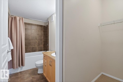 Bathroom featuring a built-in bathtub with shower, tiled surround, and wood-finish vanity with an integrated sink - 614 10503 98 Avenue, Edmonton, AB - Indoor Photo Showing Bathroom