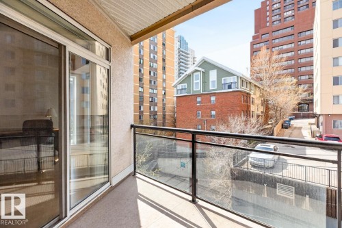 Outdoor balcony featuring a glass railing with a dark metal top rail, textured exterior wall finish, and a sliding glass door with white framing - 614 10503 98 Avenue, Edmonton, AB - Outdoor With Exterior