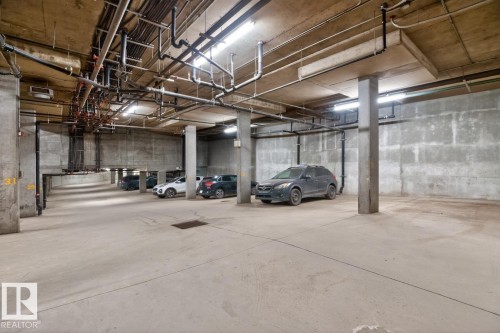 Underground parking facility featuring concrete walls, exposed ceiling pipes, and fluorescent lighting - 614 10503 98 Avenue, Edmonton, AB - Indoor Photo Showing Garage