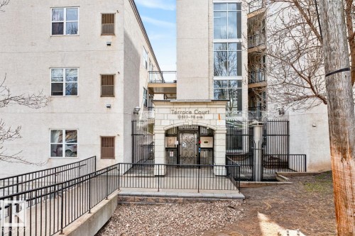 Building facade featuring a prominent arched entryway with stone detailing, an integrated ramp with metal handrails, and a multi-level window installation - 614 10503 98 Avenue, Edmonton, AB - Outdoor