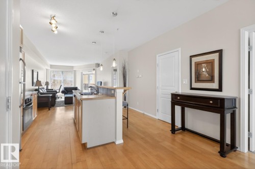 Open-concept living area featuring wood-finish flooring, a kitchen island with seating, stainless steel appliances, and a bay window - 614 10503 98 Avenue, Edmonton, AB - Indoor