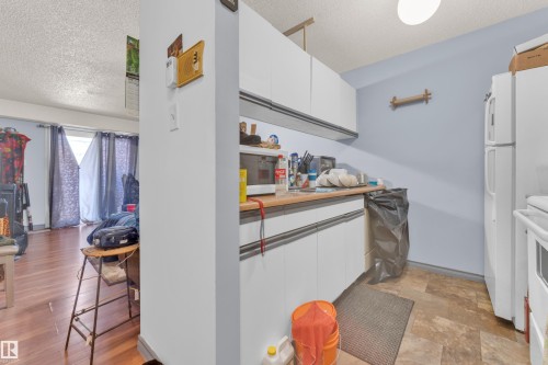 Compact kitchen area featuring white upper and lower cabinetry, a light-toned countertop, and patterned floor tiling - 101 10136 160 Street Nw, Edmonton, AB - Indoor Photo Showing Other Room