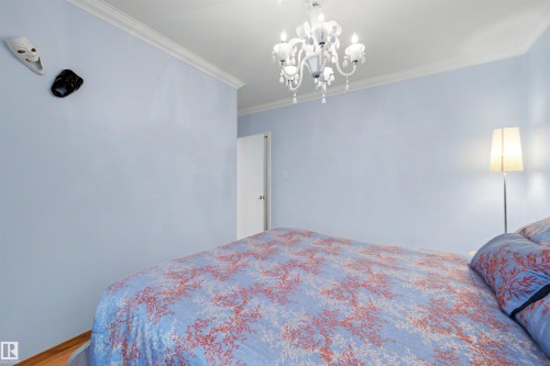 Spacious interior room featuring light blue walls, a white chandelier, crown molding, and wood-finish flooring - 9602 85 Street, Edmonton, AB - Indoor Photo Showing Bedroom