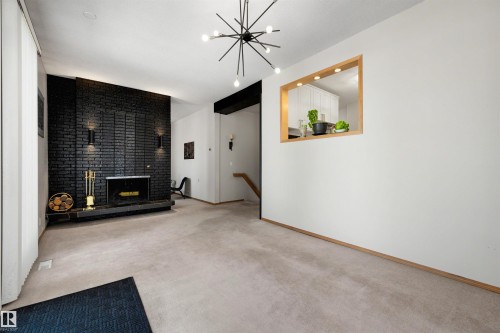 Living area featuring a black brick fireplace with a raised hearth, light carpet flooring, and a pass-through window with wood trim - 9602 85 Street, Edmonton, AB - Indoor Photo Showing Other Room With Fireplace