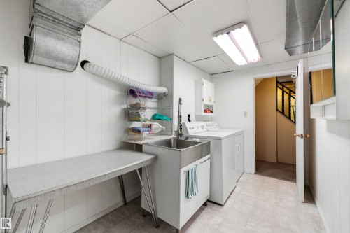 Utility room featuring a stainless steel sink, white paneled walls, a large folding surface, and tile flooring - 9602 85 Street, Edmonton, AB - Indoor Photo Showing Laundry Room