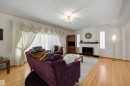 Living area featuring wood-finish flooring, a decorative fireplace with a dark mantel, glass block windows, and a multi-tiered ceiling light fixture - 9602 85 Street, Edmonton, AB  - Indoor Photo Showing Living Room With Fireplace 