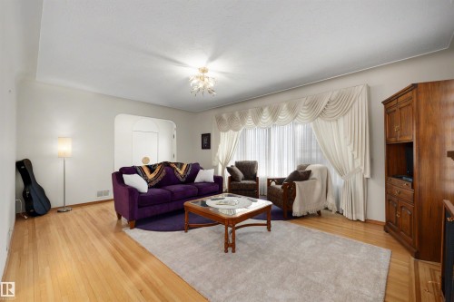 Living area featuring light wood-finish flooring, an arched doorway, a decorative ceiling fixture, and a large window with draped window treatments - 9602 85 Street, Edmonton, AB - Indoor Photo Showing Living Room