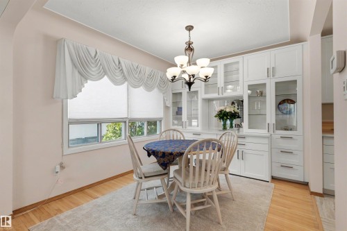 Dining area featuring extensive built-in cabinetry with glass display fronts, wood-finish flooring, a contemporary chandelier, and a window with white blinds - 9602 85 Street, Edmonton, AB - Indoor Photo Showing Dining Room