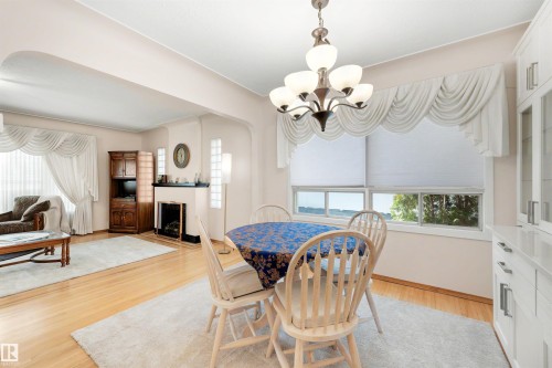 Dining area featuring a multi-bulb chandelier, a large window with roller shades, and light wood-finish flooring - 9602 85 Street, Edmonton, AB - Indoor Photo Showing Dining Room With Fireplace