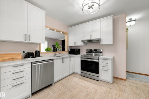 Contemporary kitchen featuring white shaker cabinetry, stainless steel appliances, light-toned countertops, a stainless steel sink with a gooseneck faucet, and wood-finish flooring in a herringbone pattern - 9602 85 Street, Edmonton, AB - Indoor Photo Showing Kitchen With Double Sink
