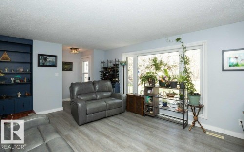 Spacious living area featuring large picture windows, wood-finish flooring, a built-in shelving unit, a wall-mounted light fixture, and light-toned wall paint - 27132A Twp Rd 632, Rural Westlock County, AB - Indoor Photo Showing Living Room