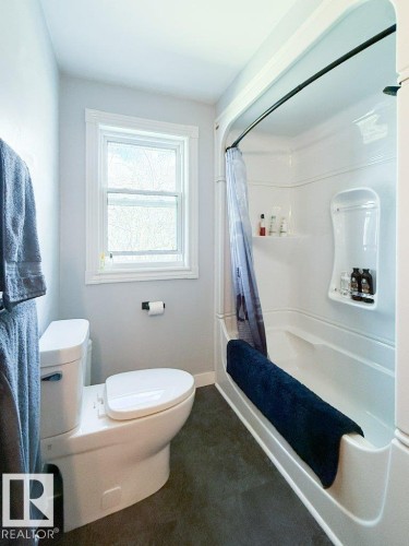 White bathtub and shower combination unit with built-in shelving, complemented by a curved shower rod - 27132A Twp Rd 632, Rural Westlock County, AB - Indoor Photo Showing Bathroom