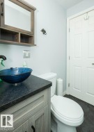 Powder room featuring a wood-finish vanity with a dark countertop and vessel sink - 