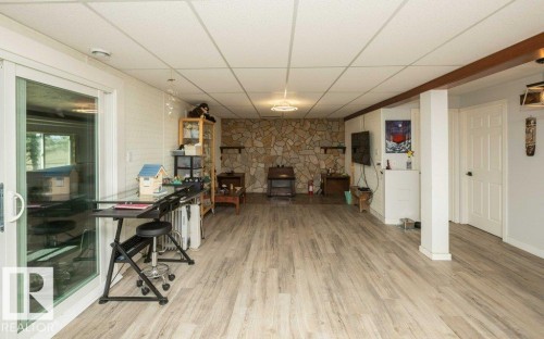 Spacious room featuring light wood-finish flooring, a full stone-faced accent wall, and a drop panel ceiling - 27132A Twp Rd 632, Rural Westlock County, AB - Indoor