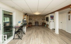 Spacious room featuring light wood-finish flooring, a full stone-faced accent wall, and a drop panel ceiling - 