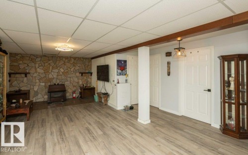 Spacious room featuring wood-finish flooring, a stone-accented wall, and multiple paneled doors - 27132A Twp Rd 632, Rural Westlock County, AB - Indoor With Fireplace
