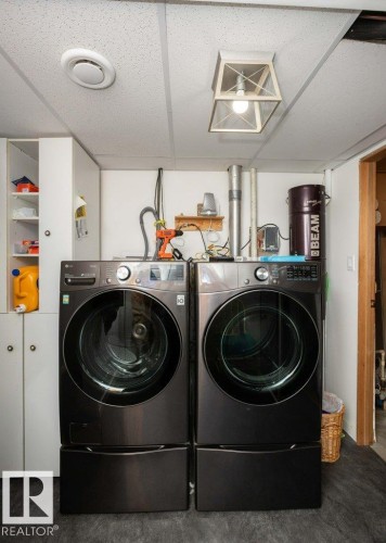 Dedicated laundry area featuring a front-loading washer and dryer set on pedestals, white cabinetry, a drop ceiling, and surface-mounted lighting - 27132A Twp Rd 632, Rural Westlock County, AB - Indoor Photo Showing Laundry Room