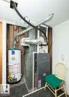 Utility closet featuring a water heater, furnace, and exposed ductwork - 