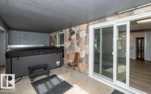 Covered outdoor patio area featuring a stone accent wall, concrete flooring, and sliding glass doors - 27132A Twp Rd 632, Rural Westlock County, AB - Outdoor With Exterior