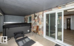Covered outdoor patio area featuring a stone accent wall, concrete flooring, and sliding glass doors - 