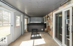 Enclosed patio featuring a hot tub, stone accent wall, concrete flooring, and sliding glass door access - 