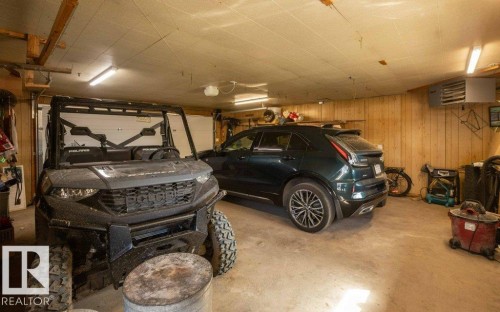 Garage interior featuring wood paneling, concrete flooring, fluorescent lighting, and an overhead garage door - 27132A Twp Rd 632, Rural Westlock County, AB - Indoor Photo Showing Garage