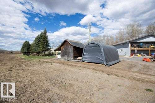 Expansive property featuring a large open field, mature evergreen trees, a rustic wooden outbuilding, and a contemporary grey metal building with an exterior balcony - 27132A Twp Rd 632, Rural Westlock County, AB - Outdoor