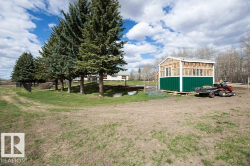 Detached outbuilding with green paneling and upper framing, set on a sizable plot with mature evergreen trees and a partially fenced perimeter - 27132A Twp Rd 632, Rural Westlock County, AB - Outdoor
