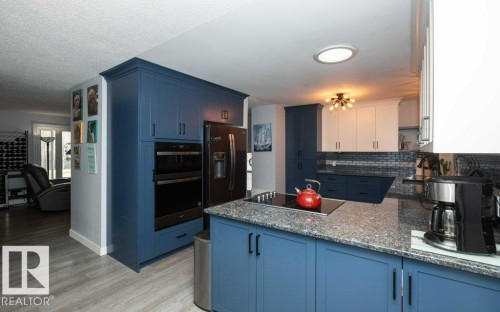 Kitchen featuring blue and white cabinetry, a built-in double oven, a smooth cooktop, and speckled stone countertops - 27132A Twp Rd 632, Rural Westlock County, AB - Indoor Photo Showing Kitchen