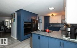Kitchen featuring blue and white cabinetry, a built-in double oven, a smooth cooktop, and speckled stone countertops - 