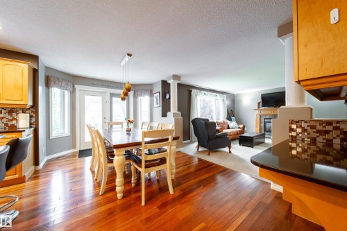 This inviting open concept interior features rich hardwood flooring, a dining area with a modern chandelier and access to exterior, and a living area with a fireplace - 4 Windrose Drive, Leduc, AB - Indoor