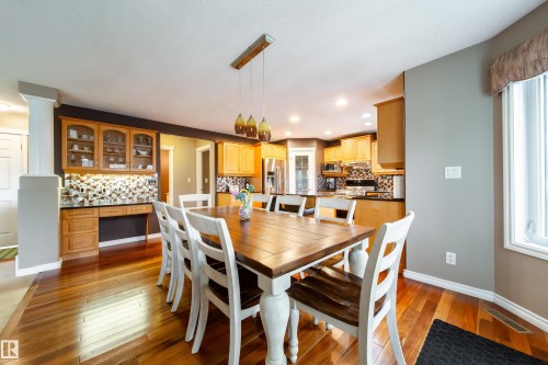 This open-concept dining area features hardwood floors, a window providing natural light, and a stylish chandelier - 4 Windrose Drive, Leduc, AB - Indoor Photo Showing Dining Room