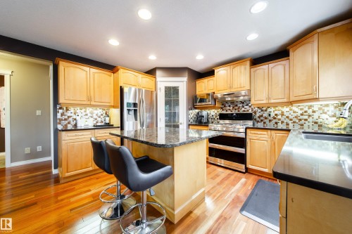 The kitchen features hardwood floors, light wood cabinetry, stainless steel appliances, and a central island with a granite countertop - 4 Windrose Drive, Leduc, AB - Indoor Photo Showing Kitchen
