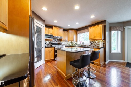 The kitchen features hardwood floors, light wood cabinetry, dark countertops, a tiled backsplash, and recessed lighting - 4 Windrose Drive, Leduc, AB - Indoor Photo Showing Kitchen