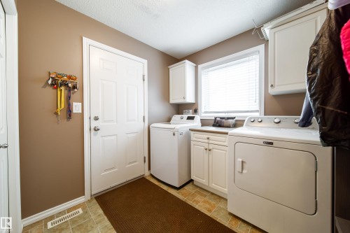 Laundry room featuring a washing machine and dryer, white cabinetry, and a window providing natural light - 4 Windrose Drive, Leduc, AB - Indoor Photo Showing Laundry Room