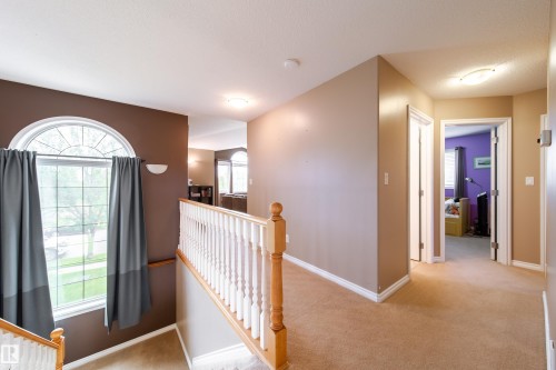 Carpeted landing area featuring a white wooden banister, an arched window with grey curtains, and neutral-toned walls - 4 Windrose Drive, Leduc, AB - Indoor Photo Showing Other Room