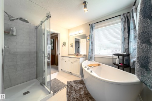 This bathroom features a spacious glass-enclosed shower with subway tile, a freestanding bathtub positioned by a window, and a vanity with a countertop and under-sink cabinetry - 4 Windrose Drive, Leduc, AB - Indoor Photo Showing Bathroom