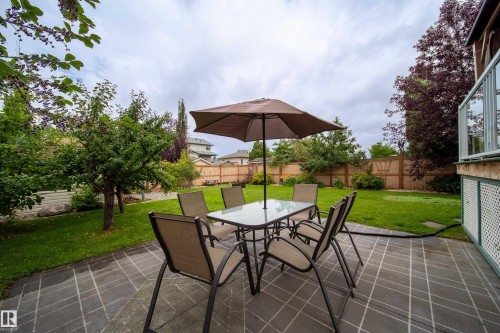 The property features a spacious paved patio area, an extensive lawn, and mature trees - 4 Windrose Drive, Leduc, AB - Outdoor With Deck Patio Veranda With Backyard
