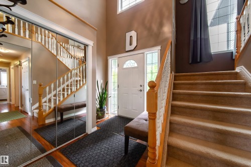 Welcoming entryway featuring a front door with decorative glass, a carpeted staircase with wood handrails, and high ceilings - 4 Windrose Drive, Leduc, AB - Indoor Photo Showing Other Room