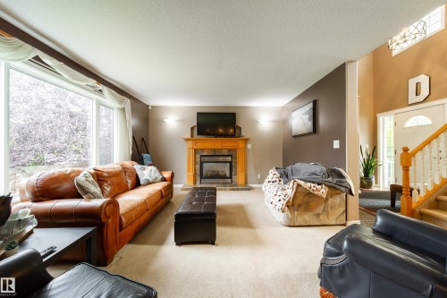 Living room featuring large windows, a fireplace with a wooden mantel, and light-colored carpeting - 4 Windrose Drive, Leduc, AB - Indoor Photo Showing Living Room With Fireplace