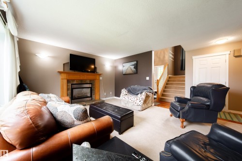 Living area featuring a fireplace with a wood mantle, an entertainment space, and a staircase with a wooden handrail - 4 Windrose Drive, Leduc, AB - Indoor Photo Showing Living Room With Fireplace