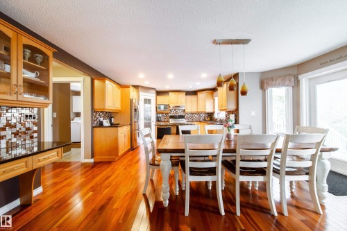 This spacious kitchen and dining area features polished hardwood flooring, extensive light wood cabinetry, a tiled backsplash, and a contemporary pendant light fixture above the dining table - 4 Windrose Drive, Leduc, AB - Indoor Photo Showing Dining Room