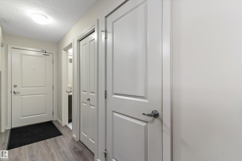 Entryway featuring wood-finish flooring, light neutral paint, and white paneled doors - 221 344 Windermere Road, Edmonton, AB - Indoor Photo Showing Other Room