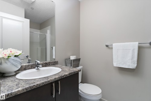 Bathroom vanity featuring a rectangular undermount sink, granite-style countertop, dark wood-finish cabinetry, and polished chrome faucet - 221 344 Windermere Road, Edmonton, AB - Indoor Photo Showing Bathroom