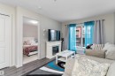 Living area featuring wood-finish flooring, a built-in electric fireplace with mantel, and a balcony with sliding glass doors - 221 344 Windermere Road, Edmonton, AB  - Indoor Photo Showing Other Room With Fireplace 