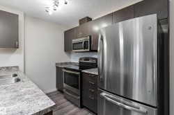 Contemporary kitchen featuring dark wood-finish cabinetry, stainless steel appliances, a subway tile backsplash, and wood-finish flooring - 