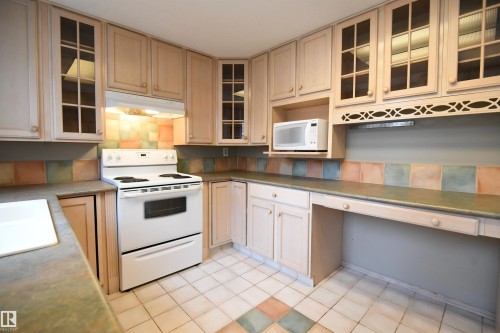 The shaker maple kitchen has loads of cabinet and counter space, and matches the extra cabinetry in the dining area.  Glass doors, ceramic tile, a writing desk, as well as an additional access to the rear yard and deck - 6706 36A Avenue, Edmonton, AB - Indoor Photo Showing Kitchen