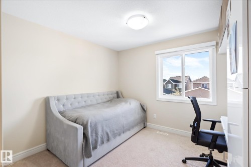 Carpeted room featuring a white-framed window, neutral painted walls, white baseboards, and a ceiling-mounted light fixture - 6864 Evans Wynd, Edmonton, AB - Indoor Photo Showing Bedroom